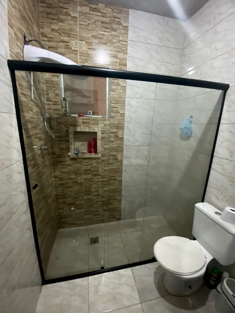 Box de vidro incolor com perfil preto num banheiro com parede de pedra